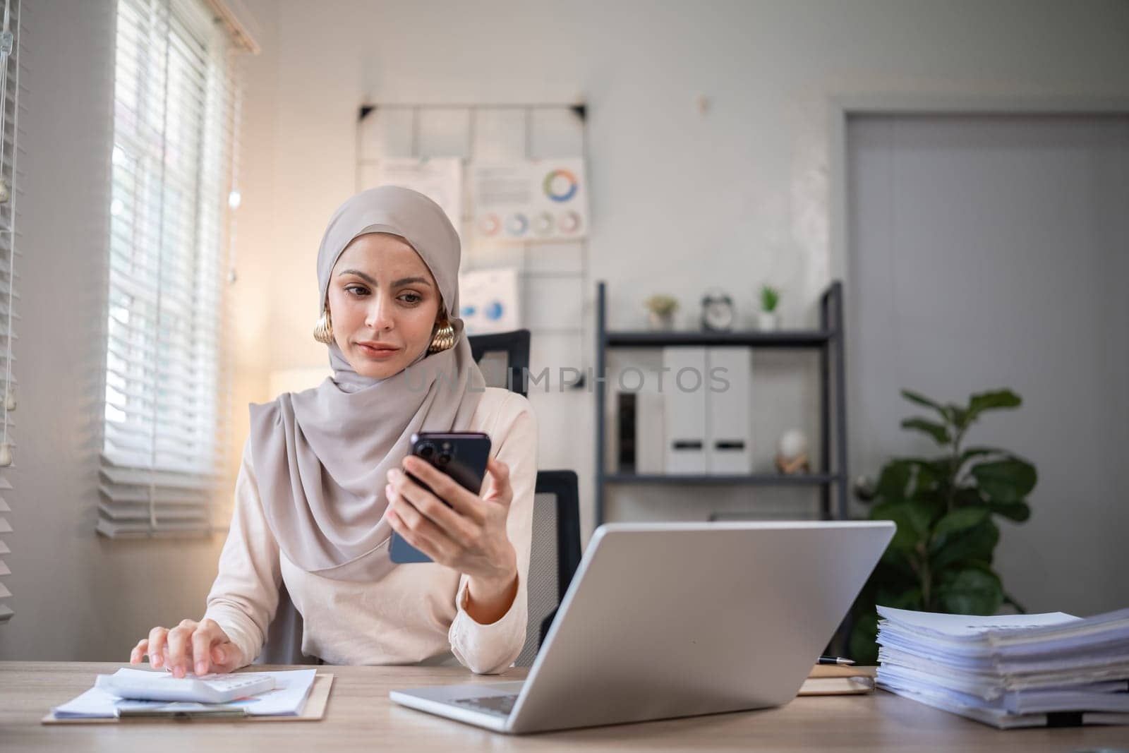 Happy Muslim businesswoman wearing hijab at work Use your laptop and smartphone to work on finance and marketing in the office. by wichayada