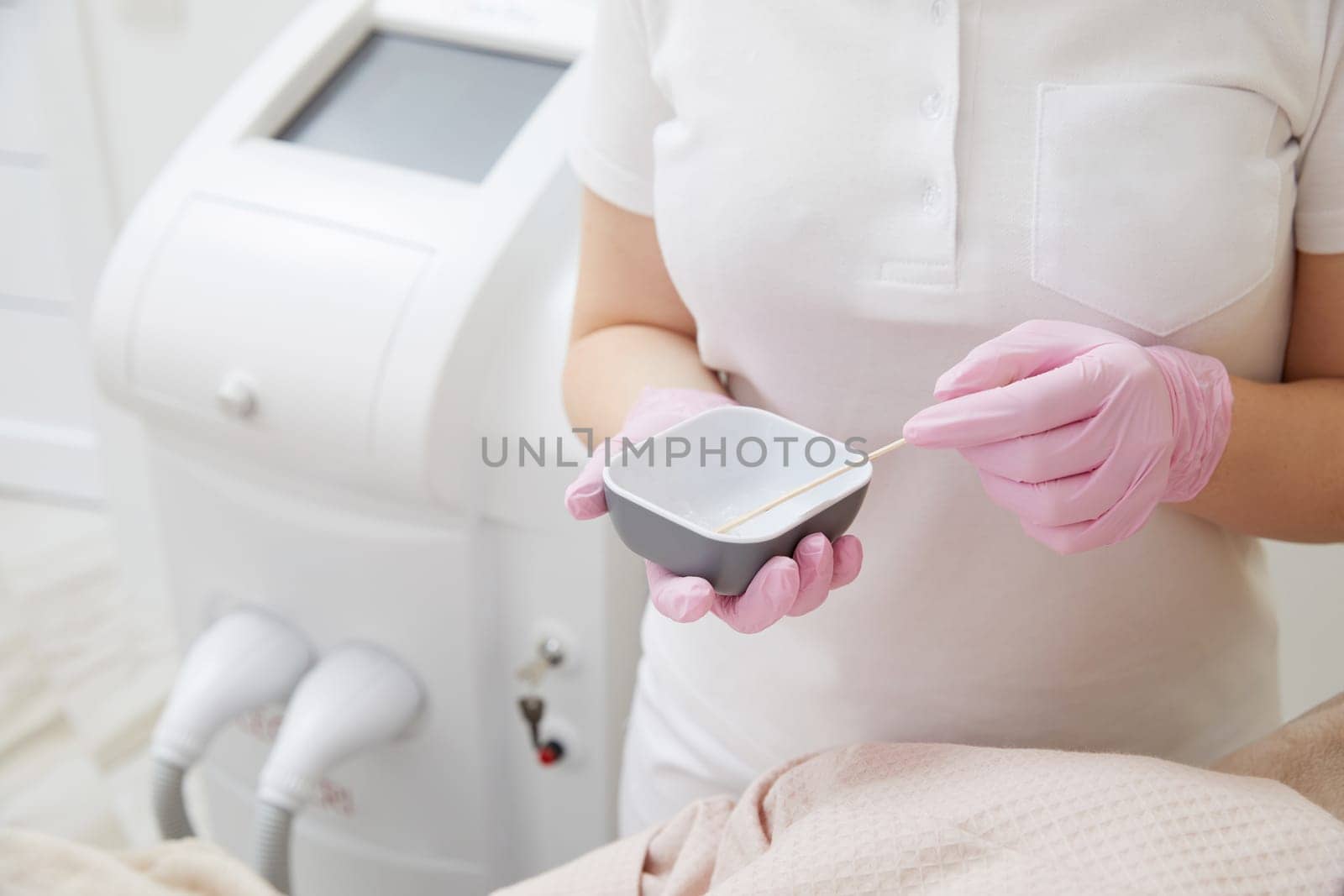 Cosmetologist applying gel before doing laser hair removal epilation on female leg in salon