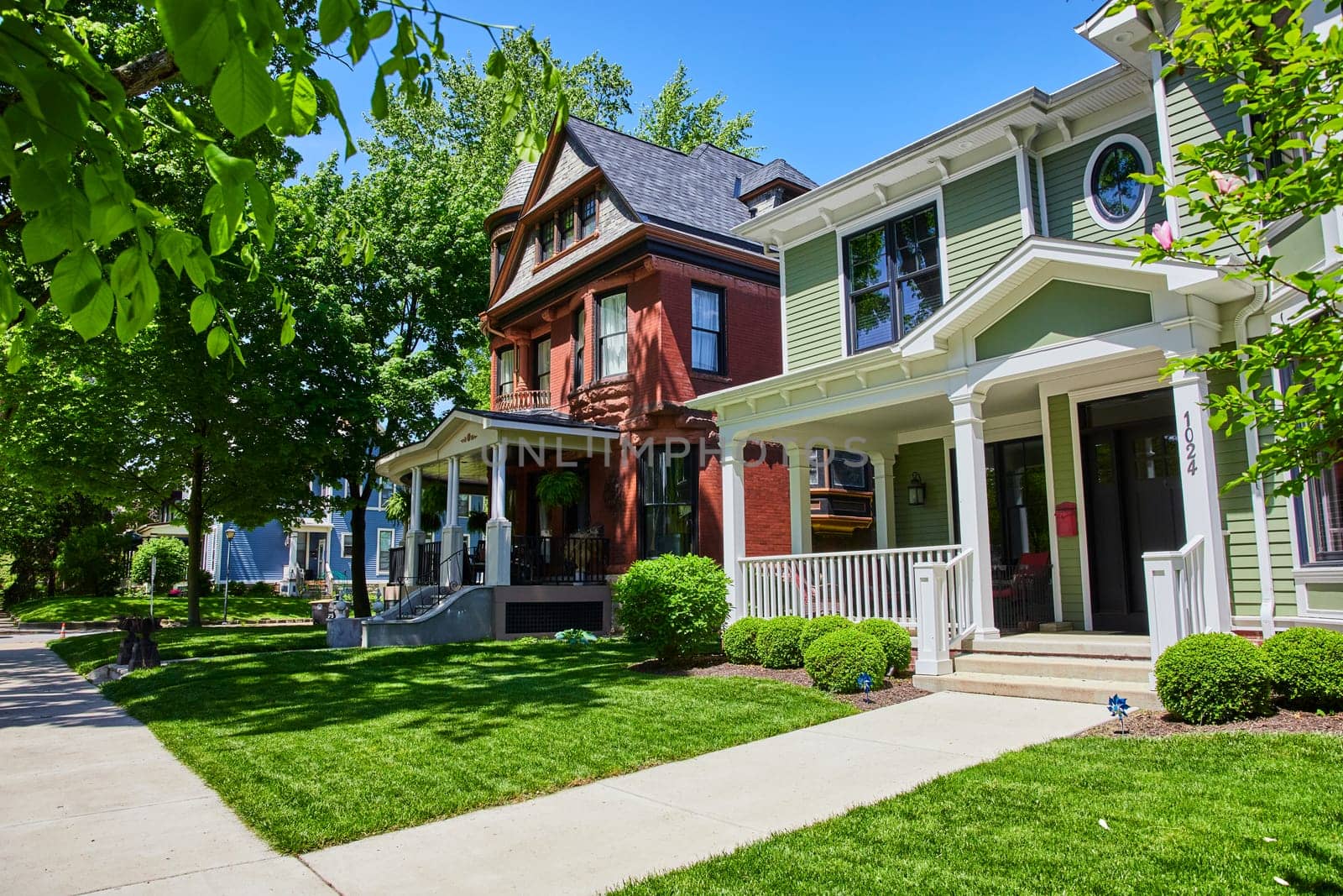 Charming suburban street in Fort Wayne with historic Victorian and modern homes under a clear blue sky.