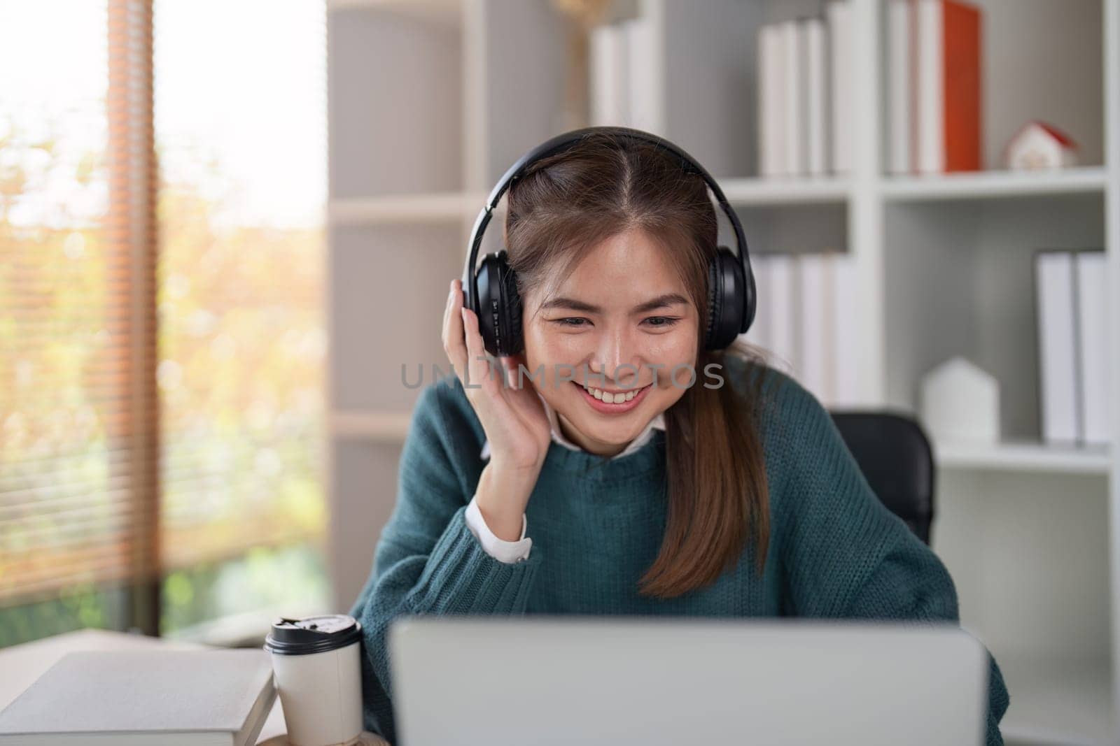 Young woman wearing headphones and smiling while using a laptop in a home office.