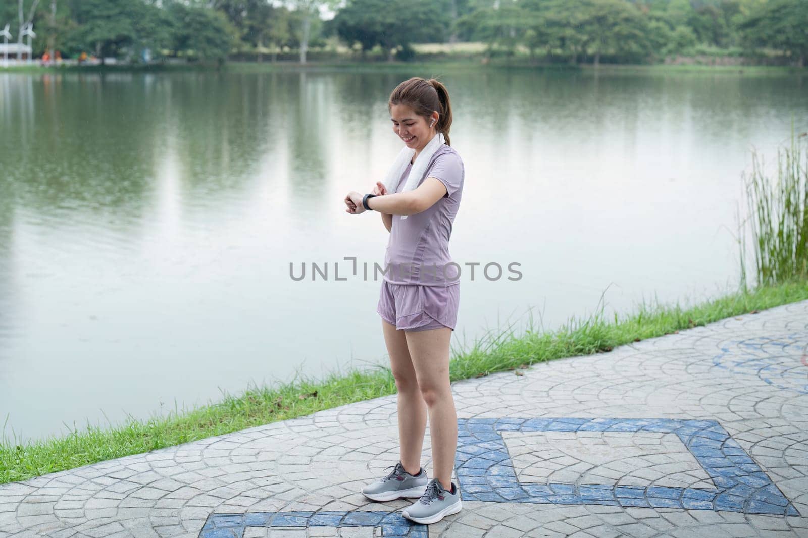 Happy young woman checking her run time on her smart watch after morning run at running park by nateemee