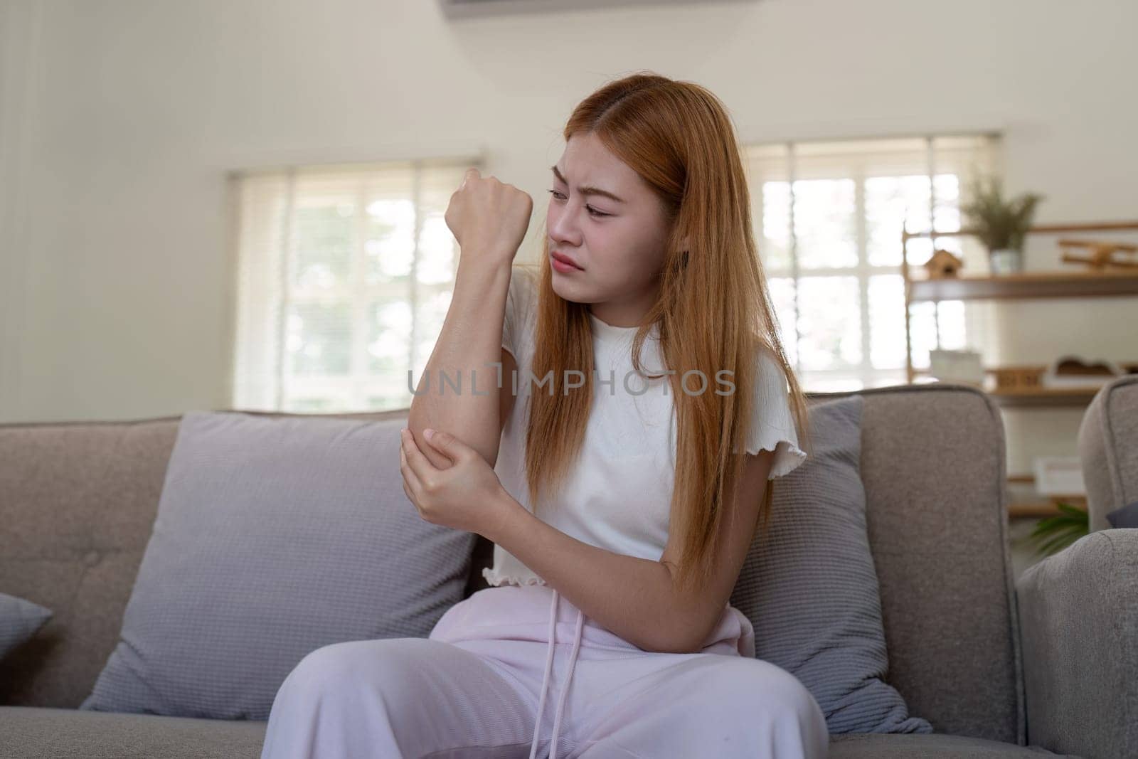 Young woman examining her arm indoors, feeling discomfort by nateemee