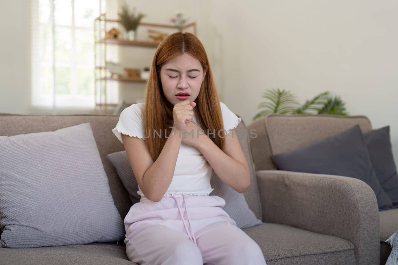 Young woman coughing while sitting on sofa at home.