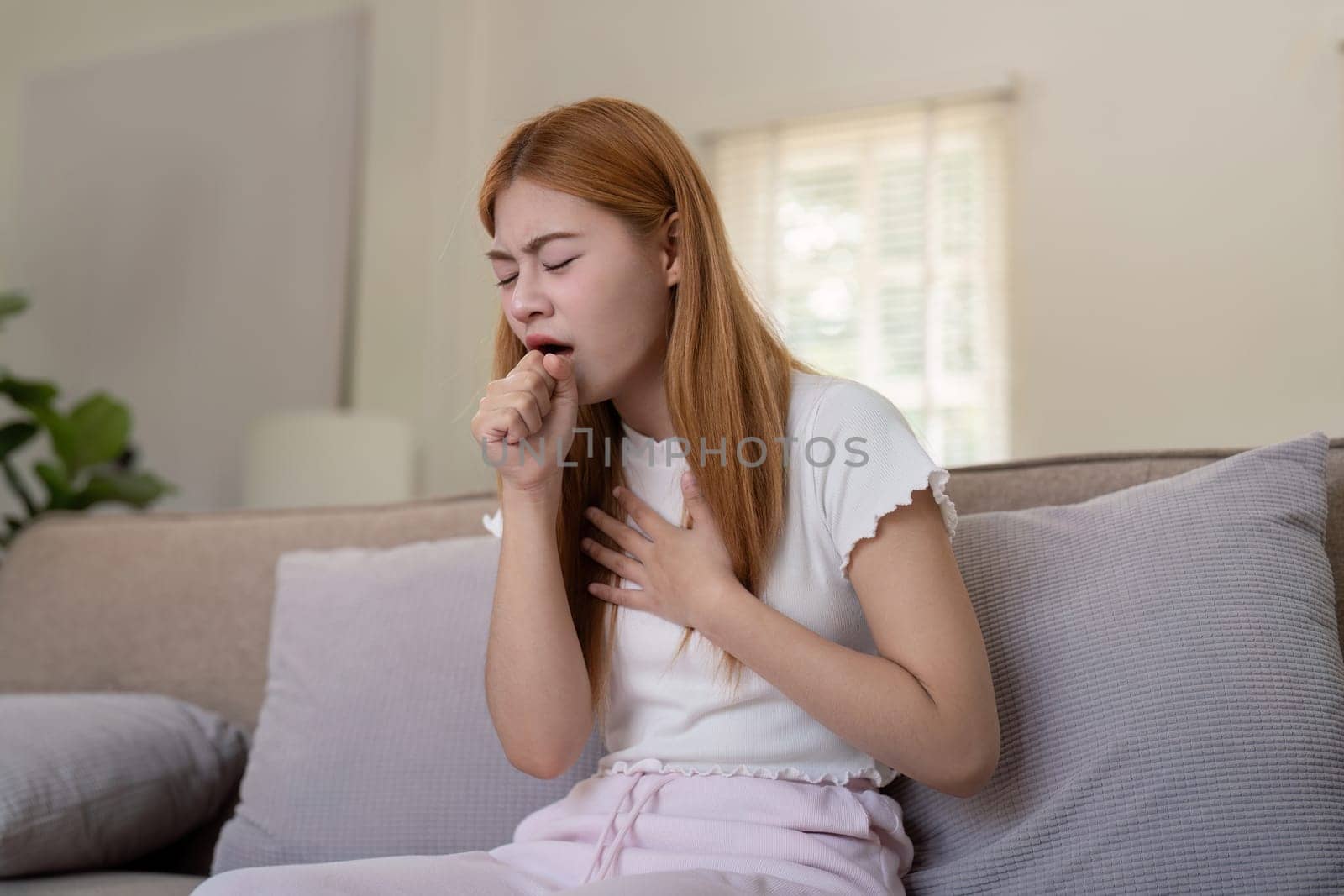 Young woman coughing while sitting on a sofa at home by nateemee