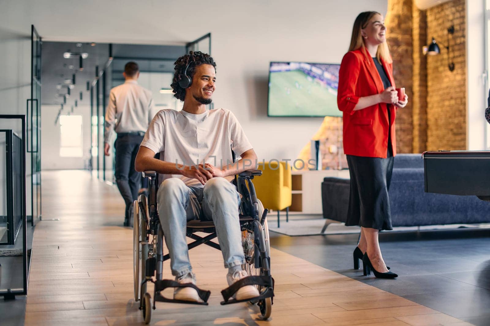 An African-American young entrepreneur in a wheelchair is surrounded by his business colleagues in a modern office setting, embodying diversity and collaboration in the workplace.