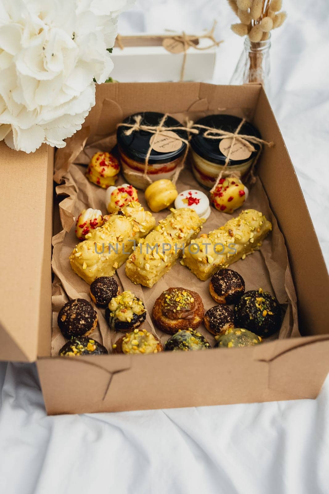 A box filled with a variety of cookies and pastries sits invitingly on a neatly made bed, creating a tempting and cozy scene.