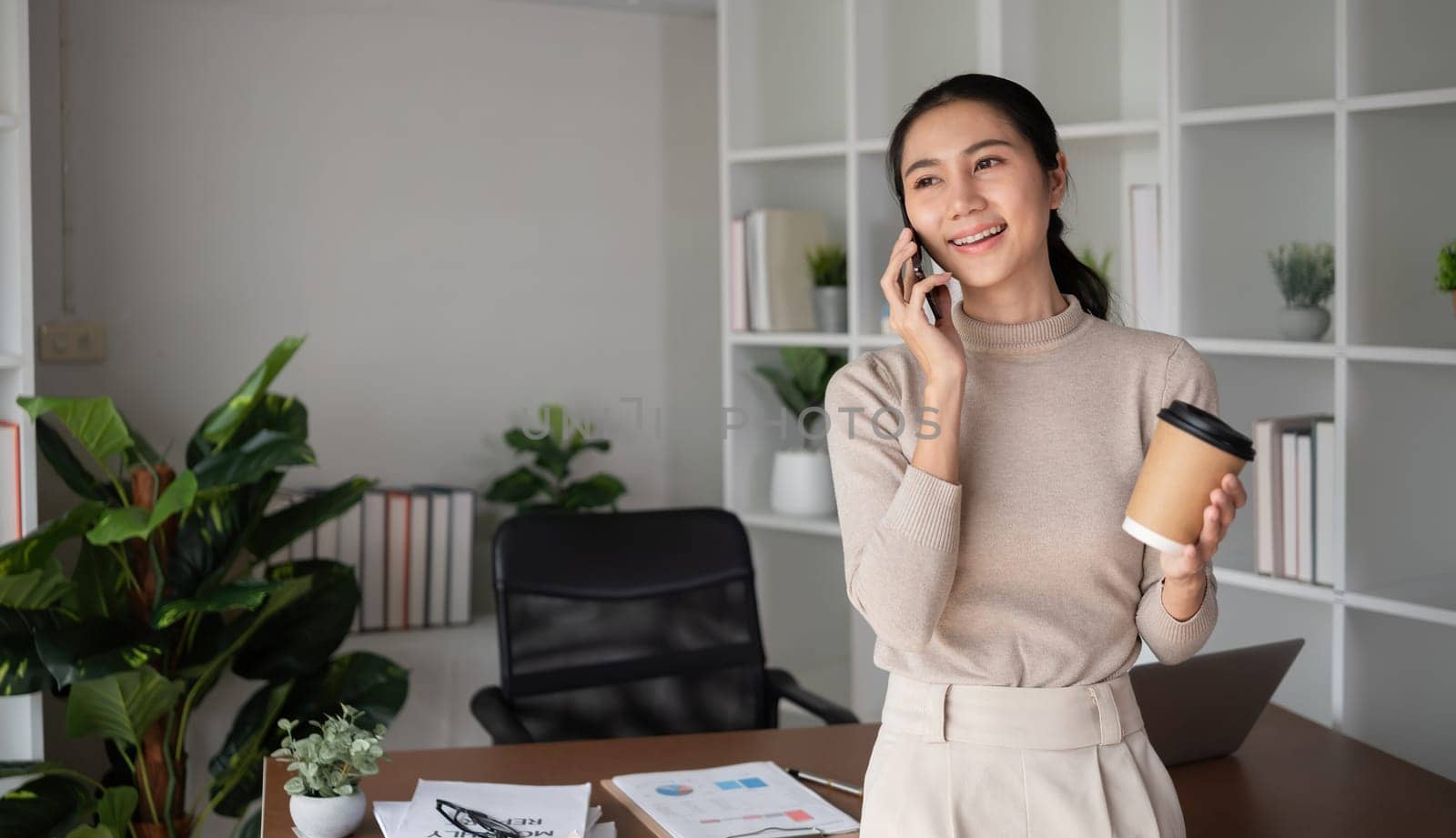 Asian businesswoman talking on the phone, having an online business meeting in a modern home office..