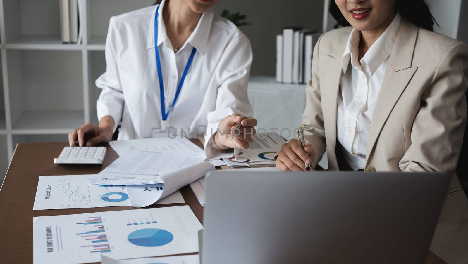 Two Asian businesswomen analyzing financial reports and graphs. Concept of financial analysis and business planning by wichayada