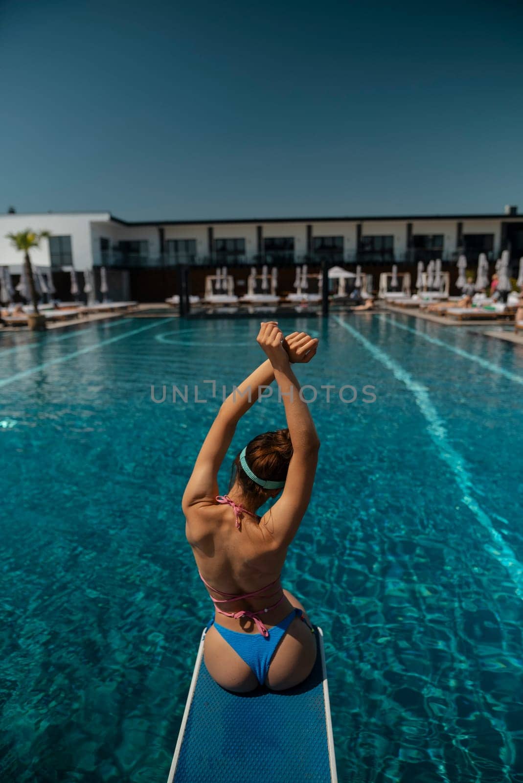 A graceful girl in a bathing suit lounges by the pool, her back to the poolside. by teksomolika