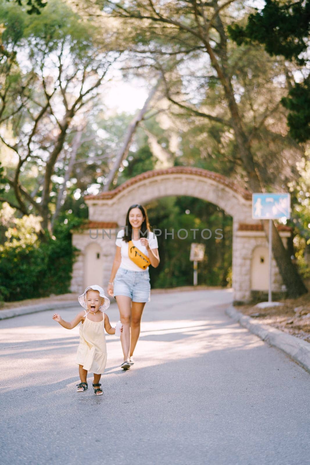 Smiling mother follows a little girl running down the road with her tongue hanging out. High quality photo