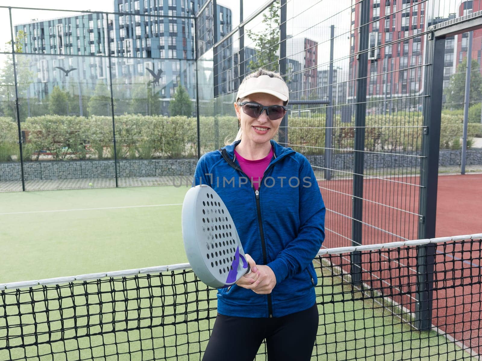 Portrait of positive young woman with racket and padel ball on tennis court. High quality photo