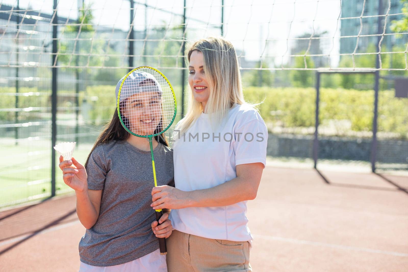 Mother and daughter are playing badminton outside in the yard on summer hot day . High quality photo