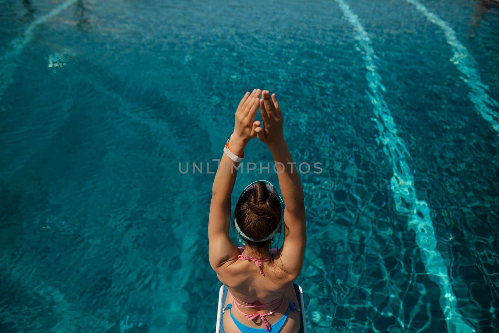 A captivating girl in a bathing suit sits by the pool, her back against the edge. High quality photo