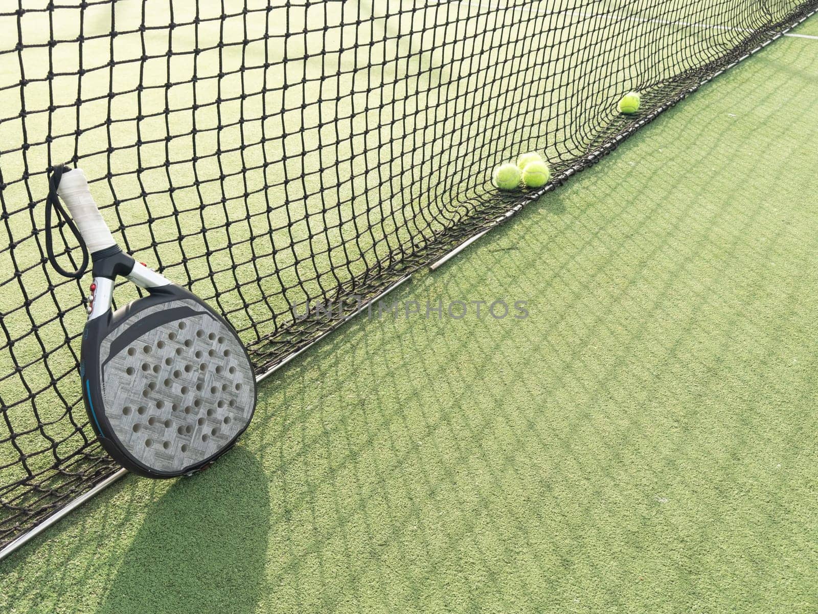 Closeup view of a paddle racket and balls in a padel tennis court near the net. Green background with white lines. Sport, health, youth and leisure concept. Sporty equipment. White lines in background. High quality photo