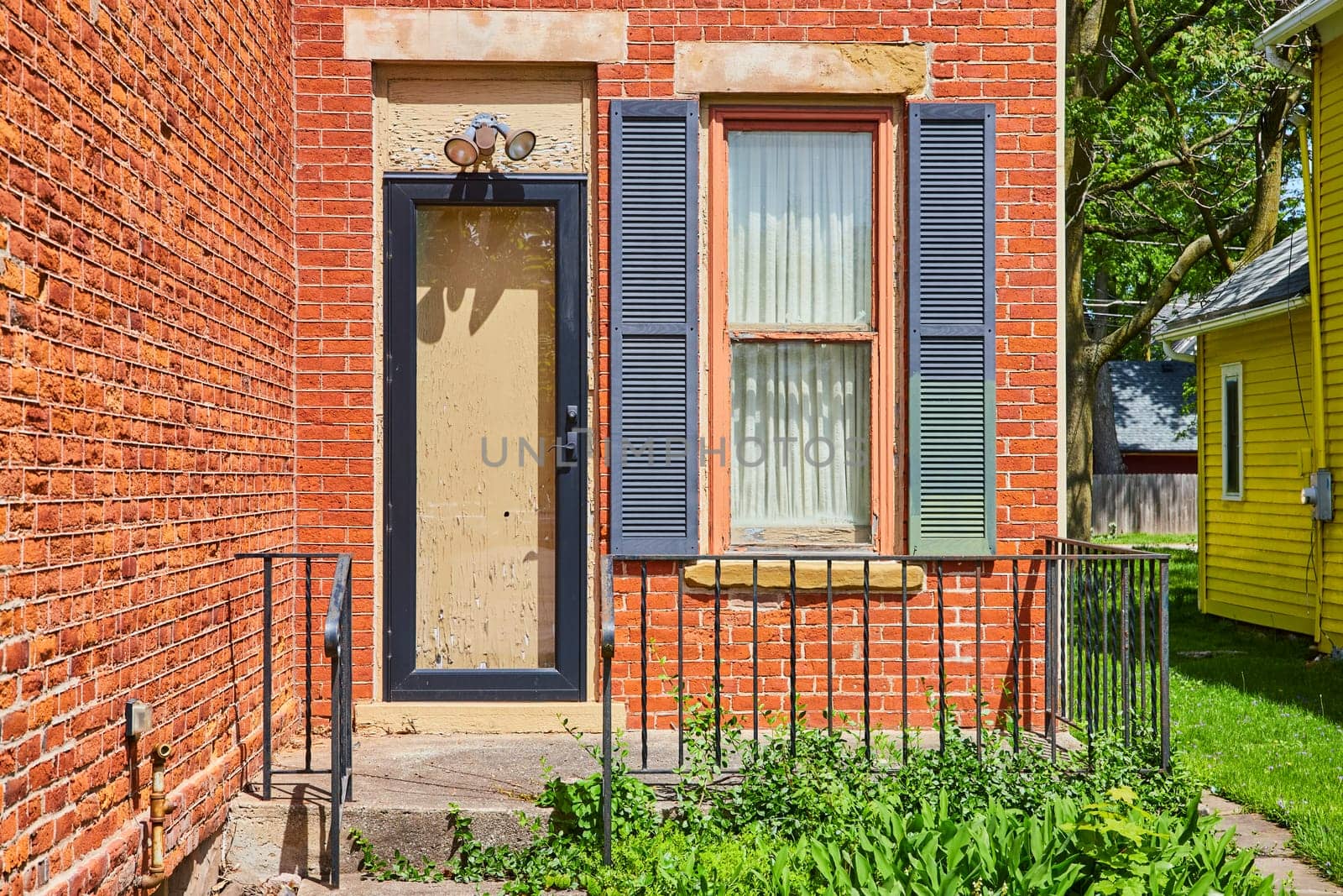 Vintage beige door and window with dark shutters set in a weathered red brick wall, Fort Wayne.