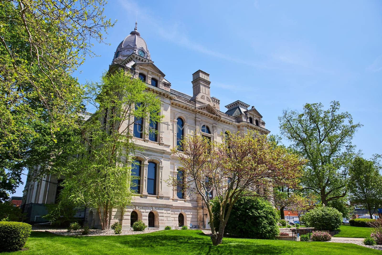 Historic Kosciusko County Courthouse in Warsaw, Indiana, framed by lush greenery under a clear blue sky.