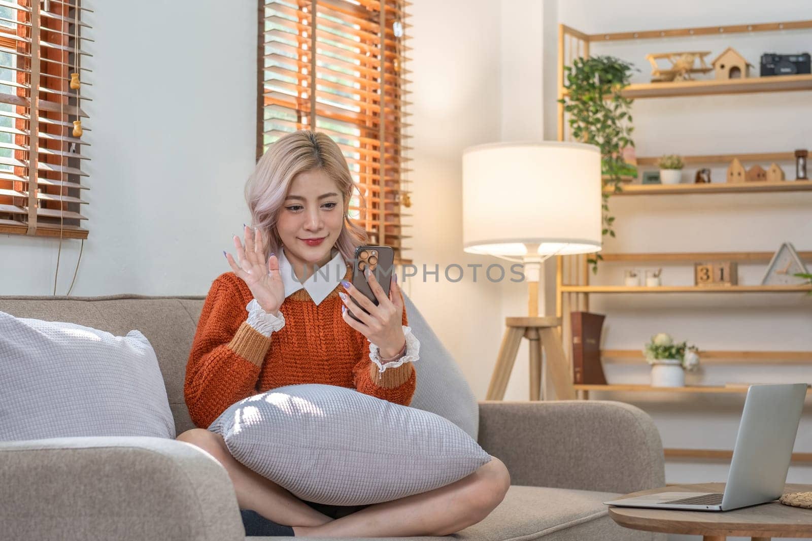 Beautiful young woman sitting on the phone, chatting with friends via video call, resting and relaxing in the living room. by wichayada