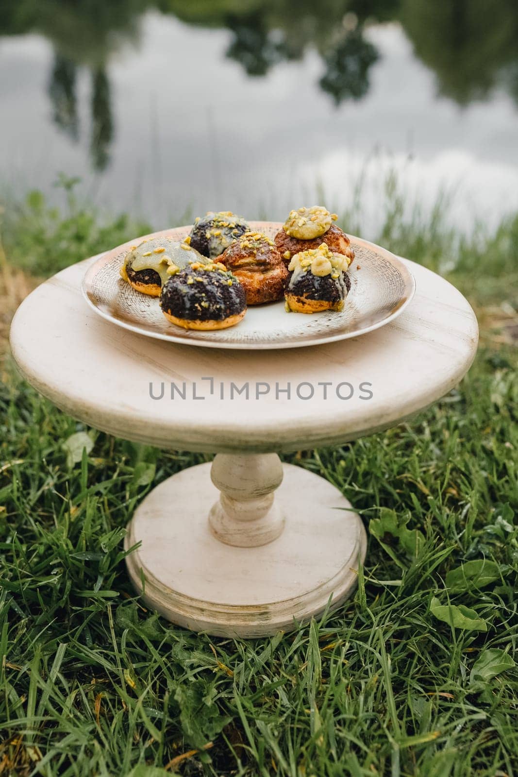 A picturesque scene of a plate of pastries laid out on the grass next to a serene body of water, inviting a tranquil afternoon picnic.