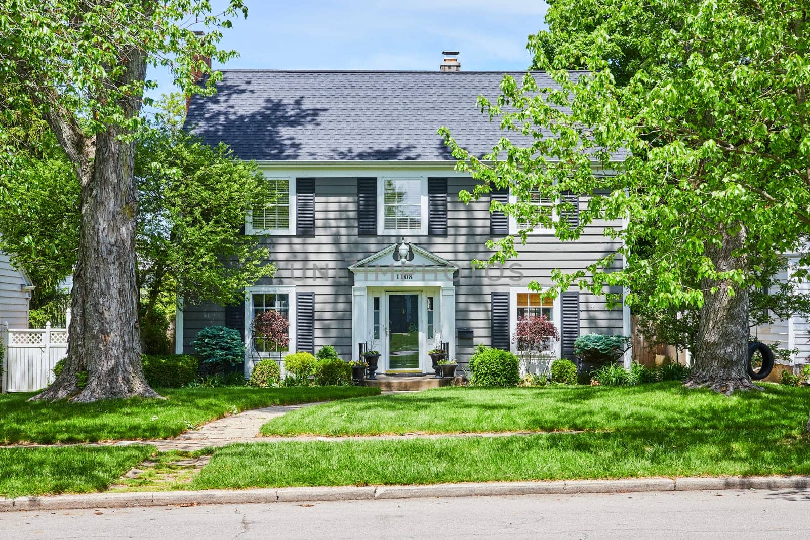 Elegant suburban home in Fort Wayne, bathed in sunlight, showcasing timeless architecture and lush greenery.