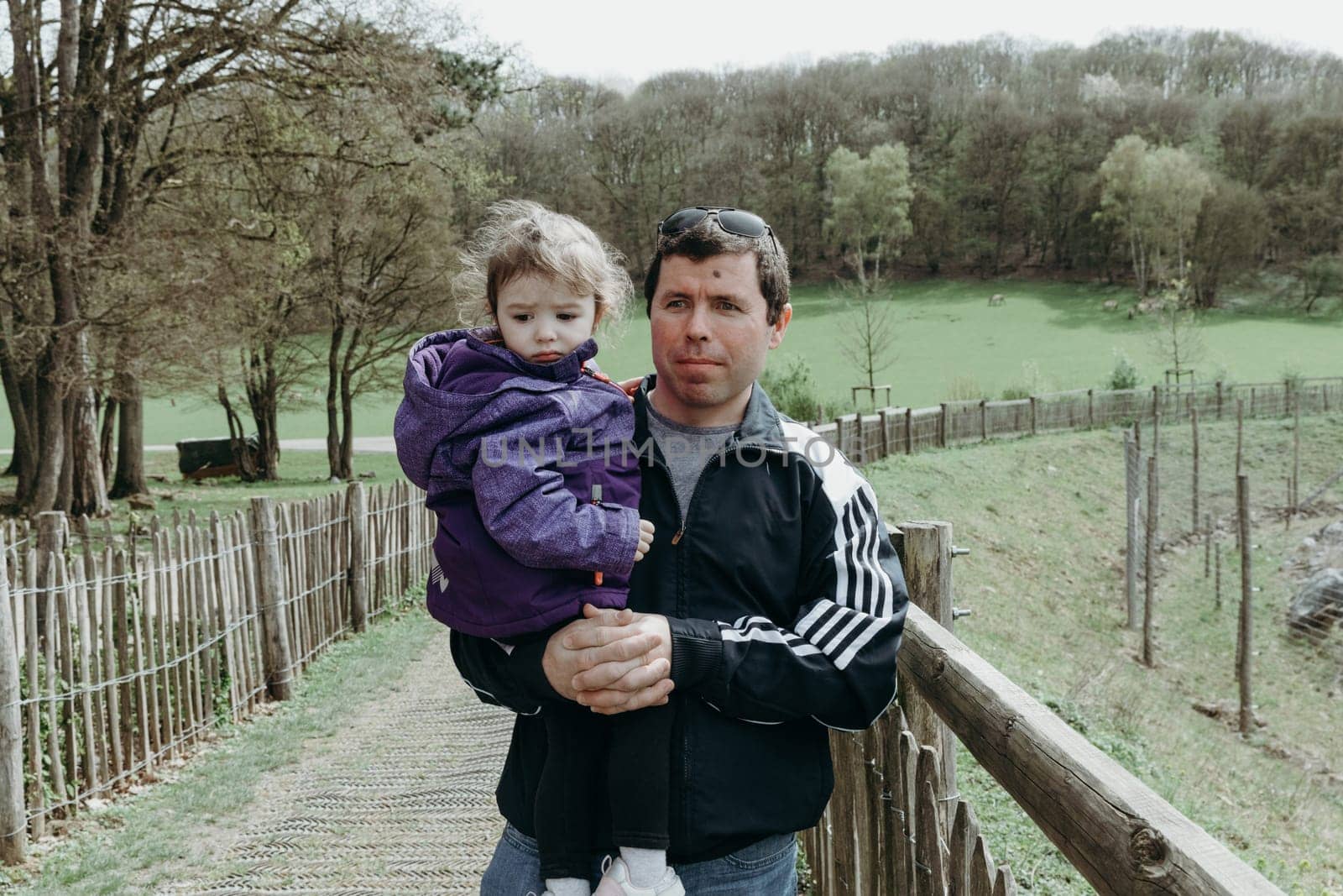 Portrait of one young handsome brunette Caucasian man holding a little girl in his arms, walking through a nature reserve in Belgium on a spring day, close-up side view.