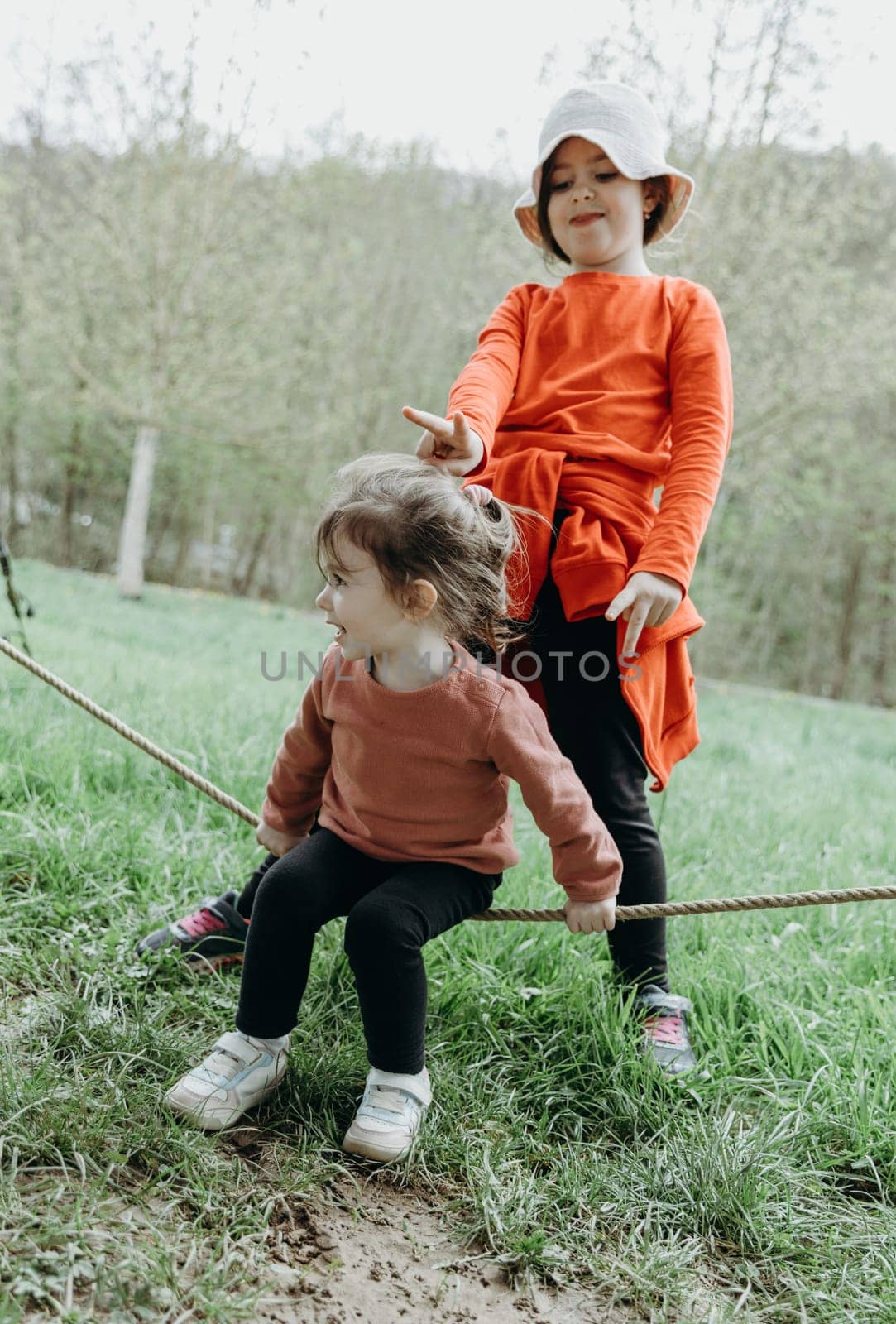 Portrait of two little beautiful Caucasian girls sisters having fun playing and fooling around with a rope on a spring day in a park in Belgium, close-up side view.