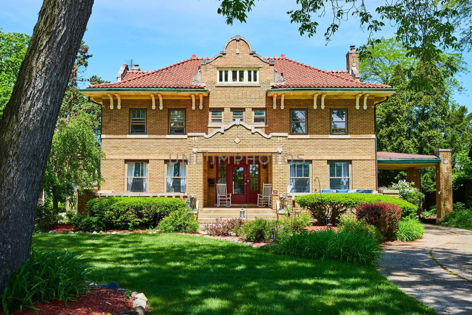 Sunny day at a historic brick home in South Wayne, Fort Wayne, showcasing early 20th-century architecture and lush landscaping.