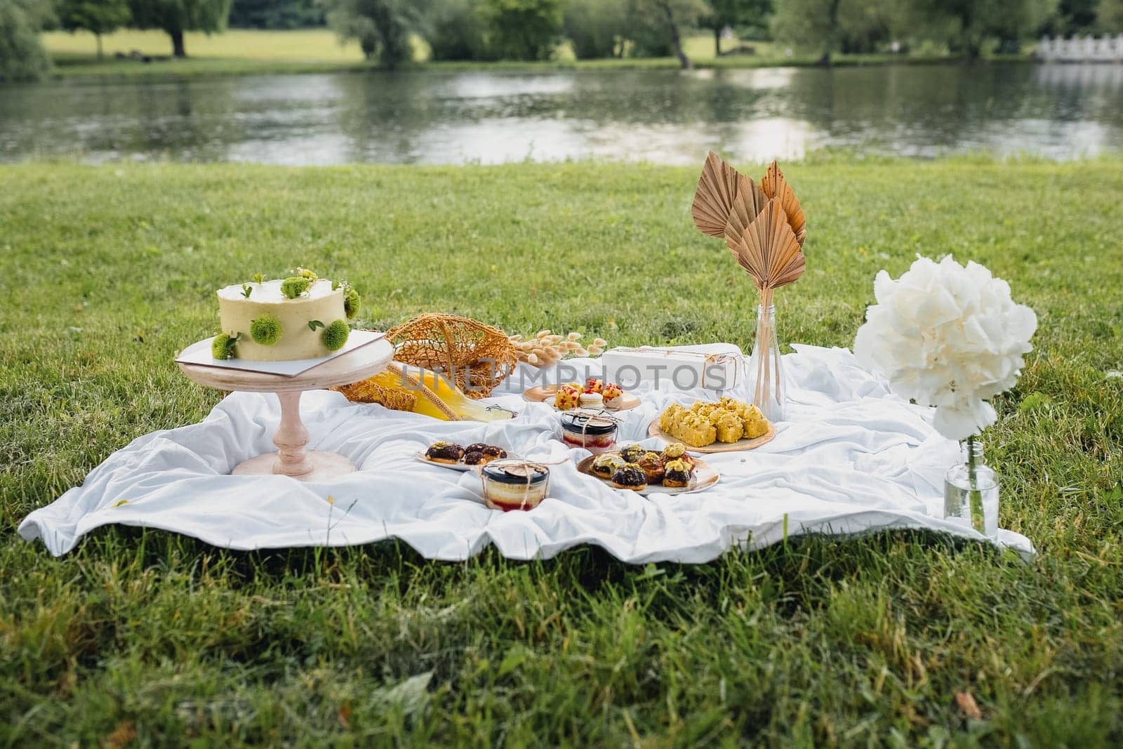 A colorful picnic blanket spread with delicious food and drinks, set up near a serene lake on a sunny day.