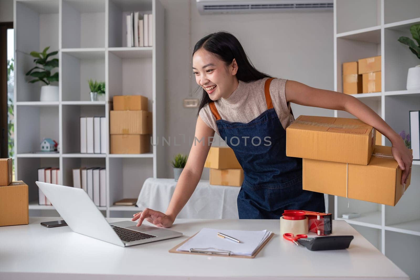 Asian women packing boxes and using a tablet in a home office. Concept of small business and e-commerce.