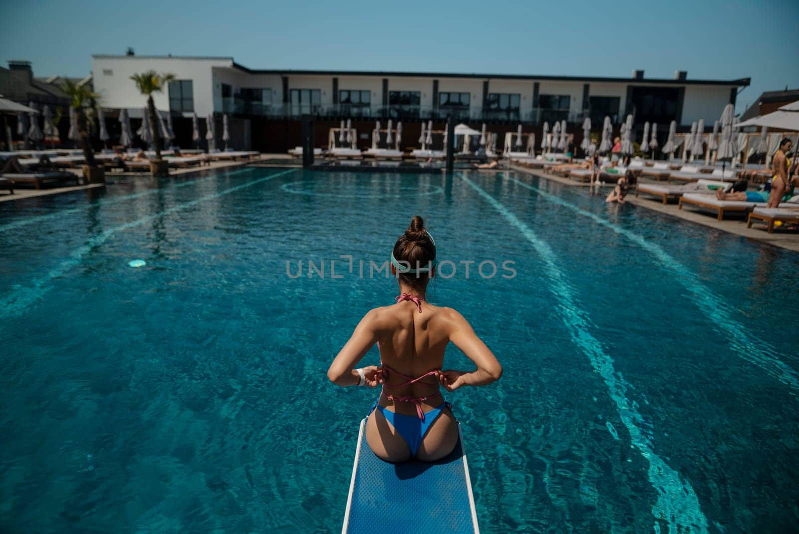 A vibrant lady, dressed in a blue bikini, stands before the pool's cerulean waters. High quality photo