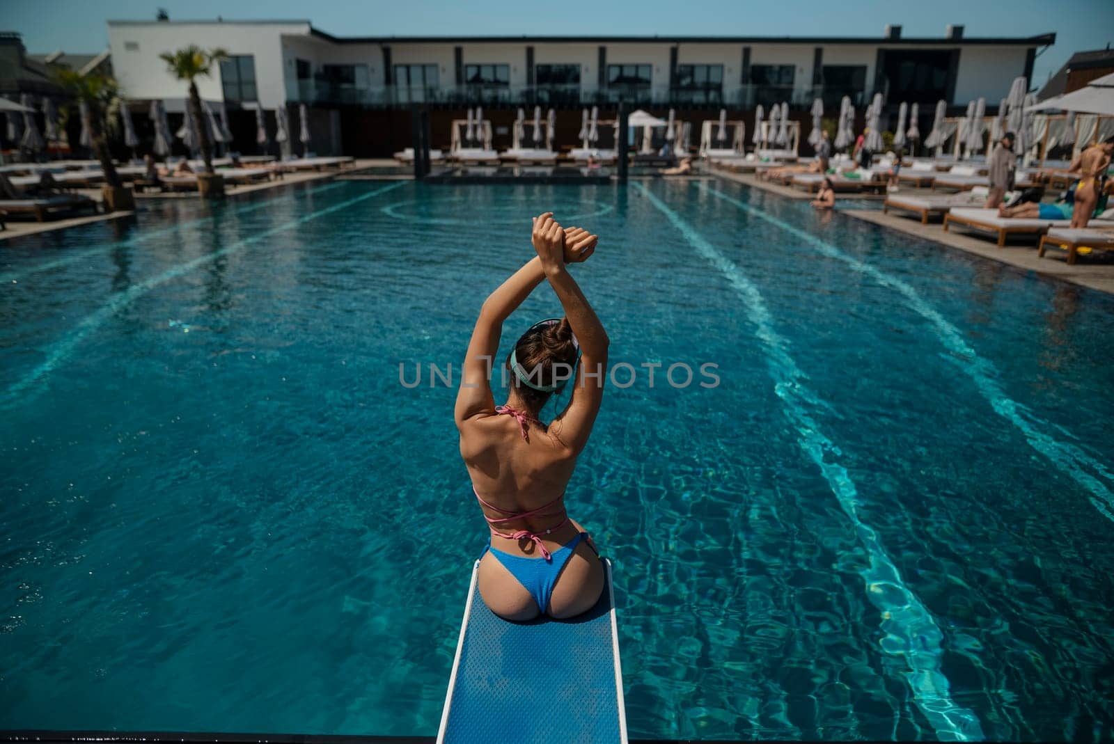 An alluring lady in swimwear reclines by the pool, with her back to the water. High quality photo