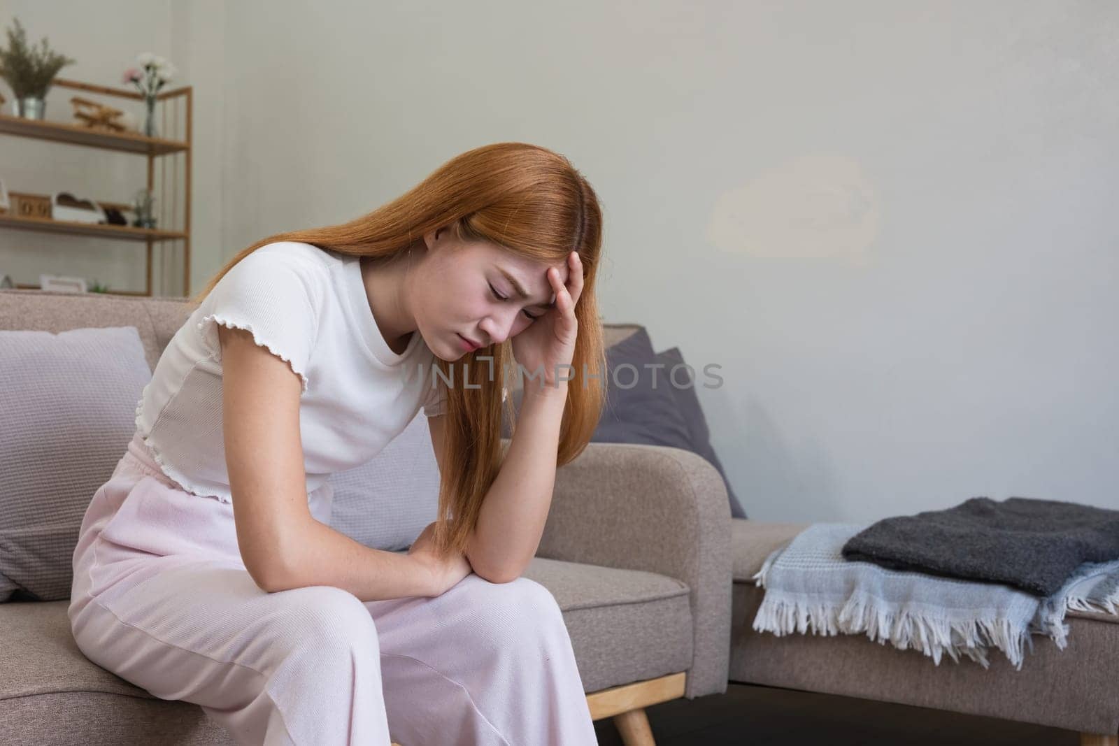 A young Asian woman in the living room was suffering from a headache due to accumulated stress due to health problems and lifestyle problems causing stress disorder. by wichayada