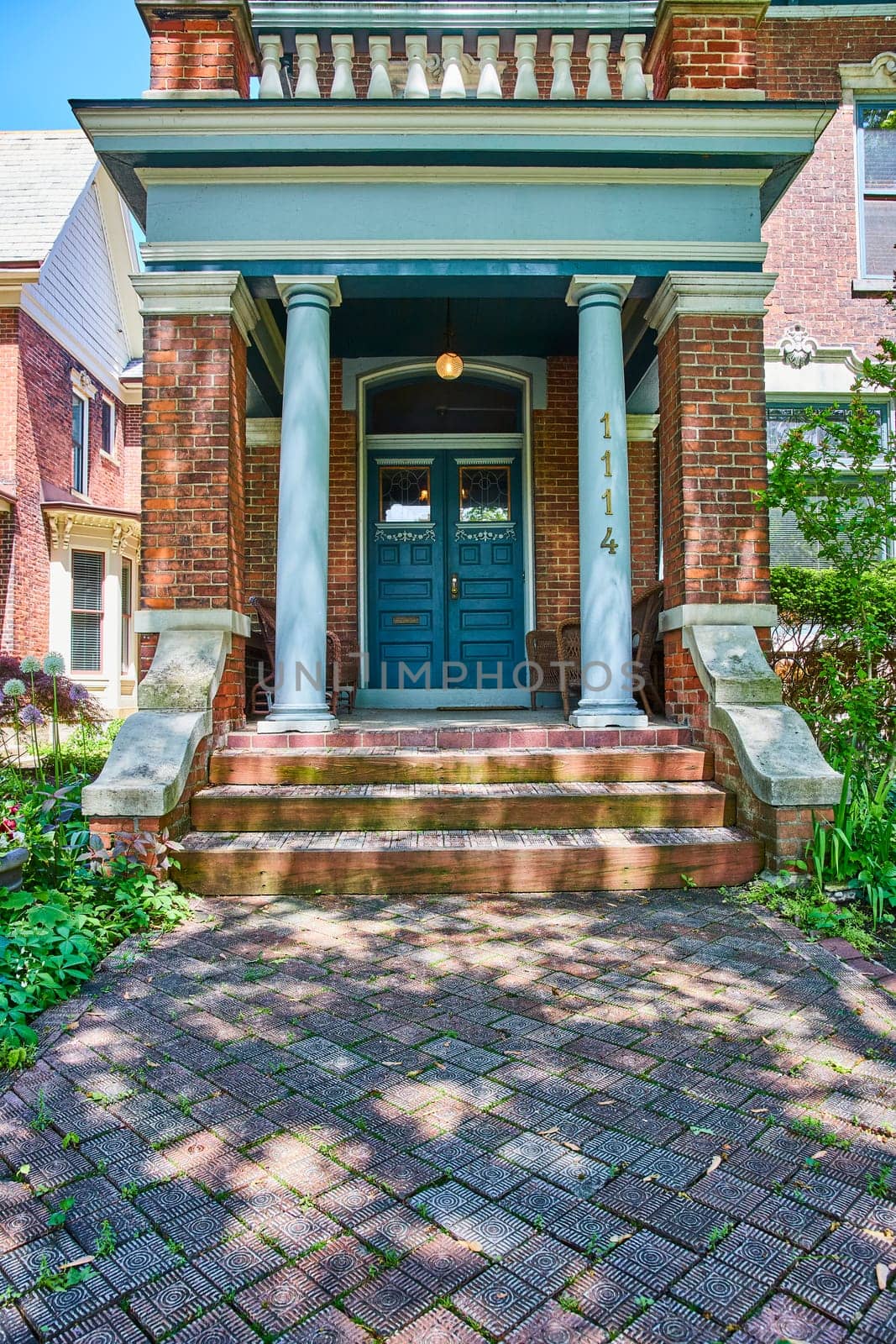 Traditional brick house with elegant porch in Fort Wayne, bathed in sunlight, evokes warmth and hospitality.