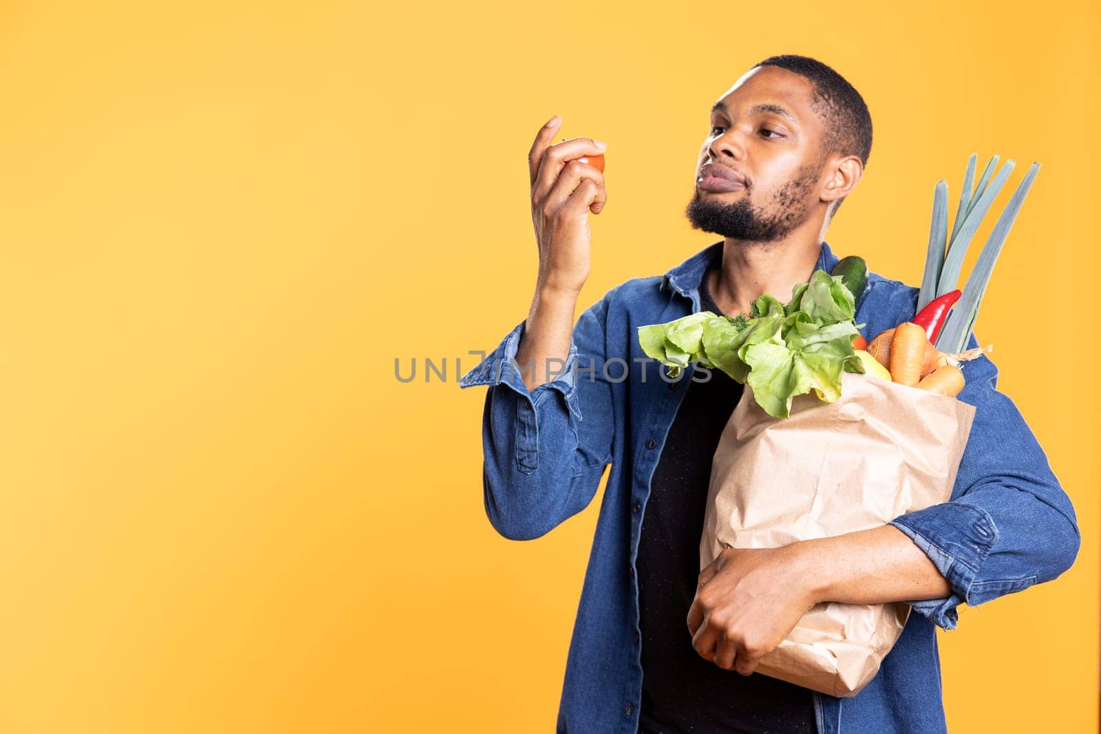 African american guy admiring a tomato and smelling the fresh aroma by DCStudio