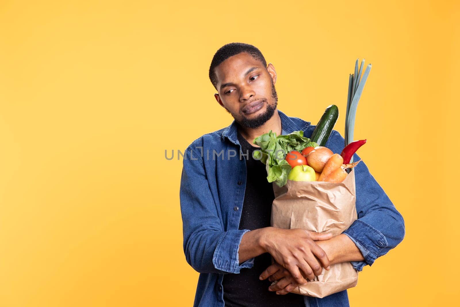 Pensive displeased young guy holds a paper bag full of bio food by DCStudio