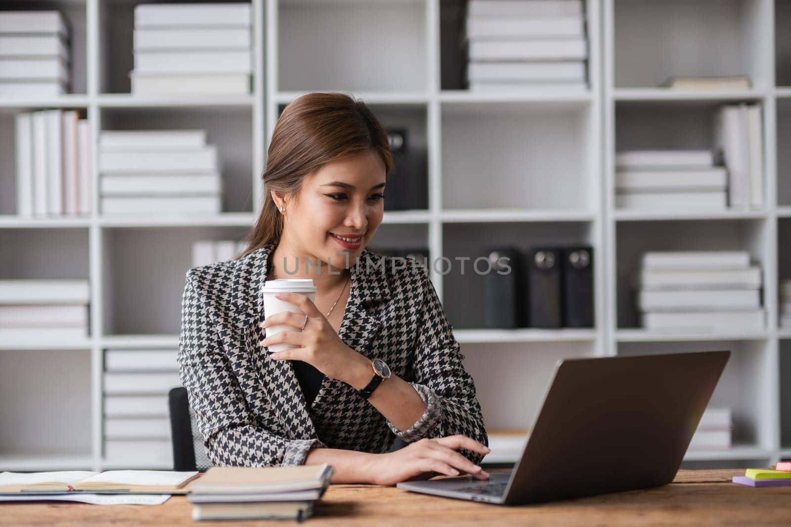 Beautiful determined business woman working using laptop and calculator calculating turnover in modern office by wichayada