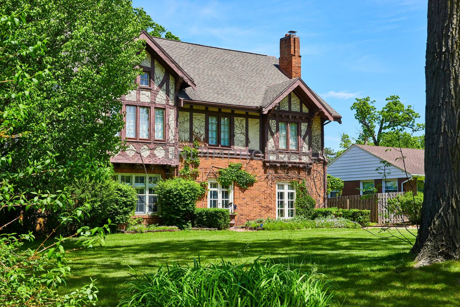 Charming Tudor-style home in South Wayne Historic District, surrounded by lush greenery under a sunny sky.