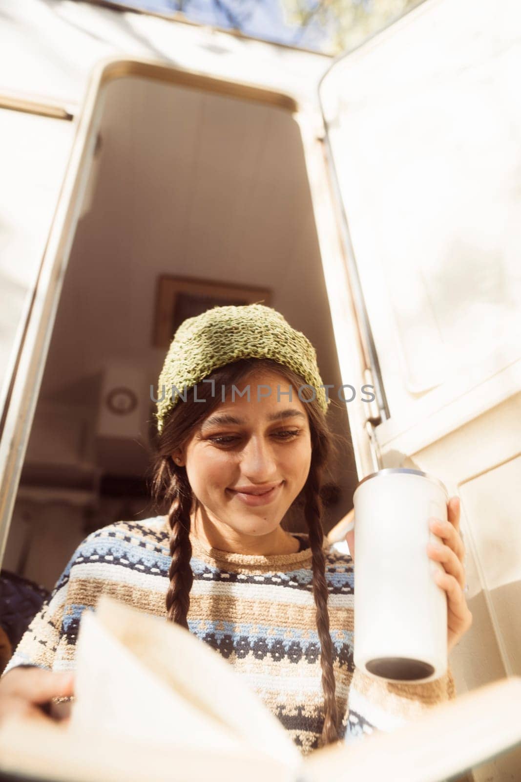 A trendy, free-spirited girl, dressed in a hippie ensemble, sips a warm drink on the terrace. High quality photo