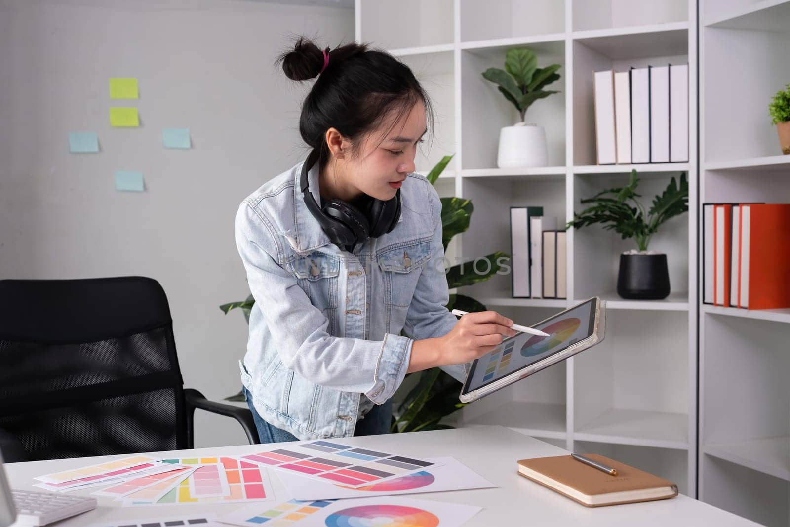 Female designer wearing headphones listening to music while doing graphic design work Choose colors for working with the computer at the table by wichayada