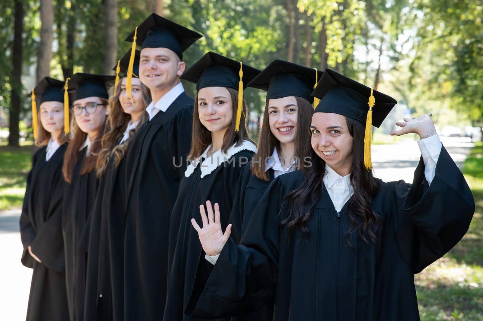 Row of happy young people in graduation gowns outdoors. Students in the park. by mrwed54