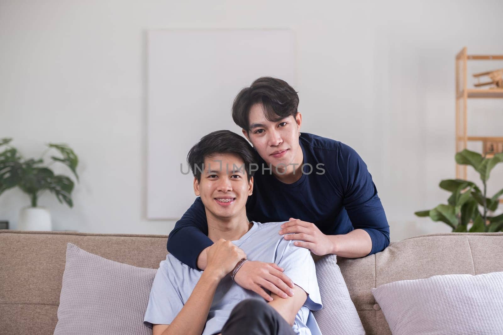 Happy Asian homosexual couple embrace on sofa in living room by wichayada