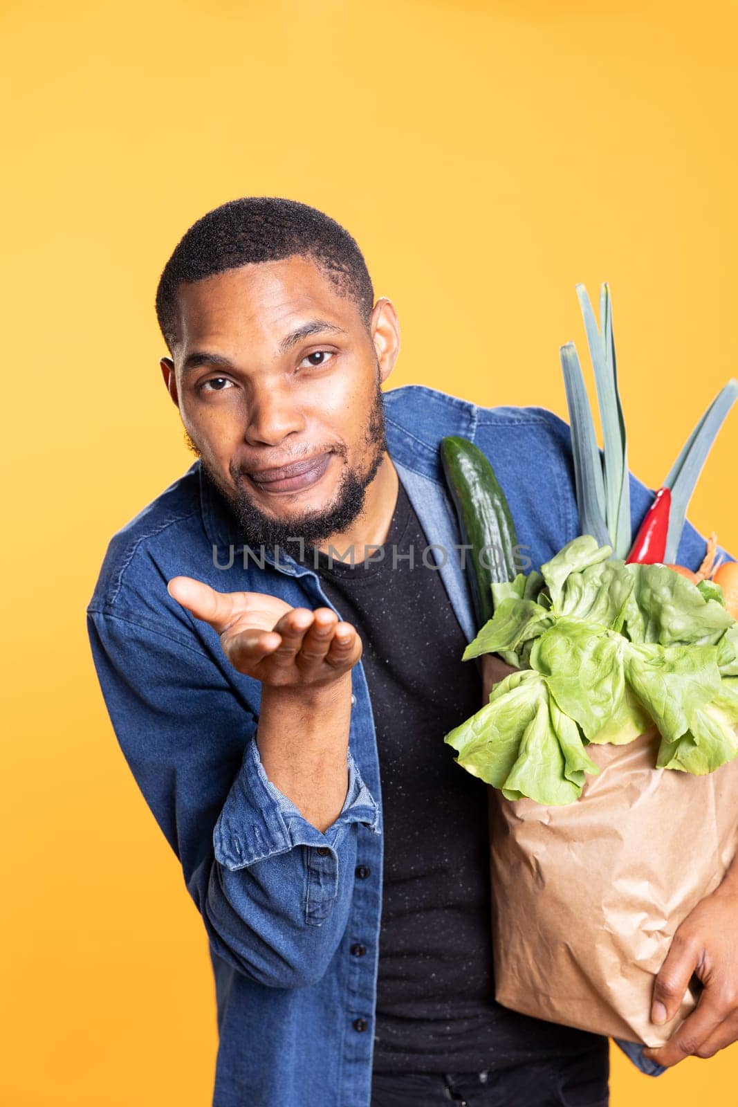 African american male model gives air kisses against yellow background, shopping for food at a local supermarket. Charismatic person supports zero waste with ethically sourced goods.