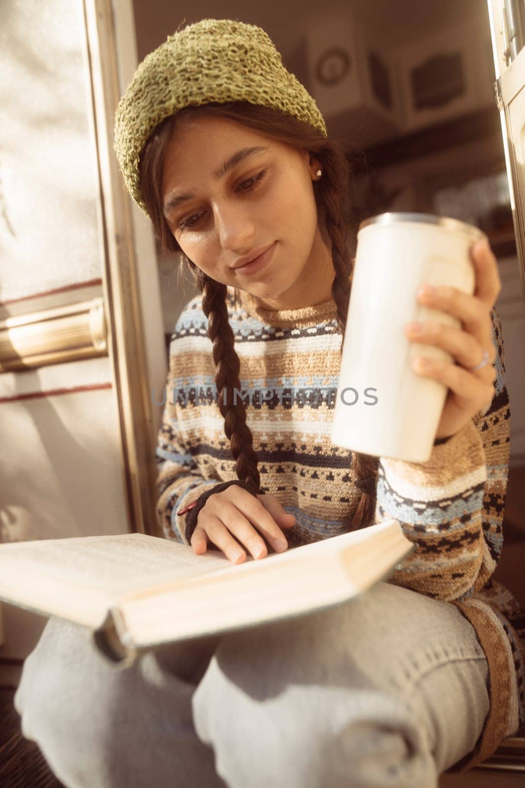 A trendy, hippie-inspired girl relishes a hot beverage on the house terrace, showcasing her style. High quality photo