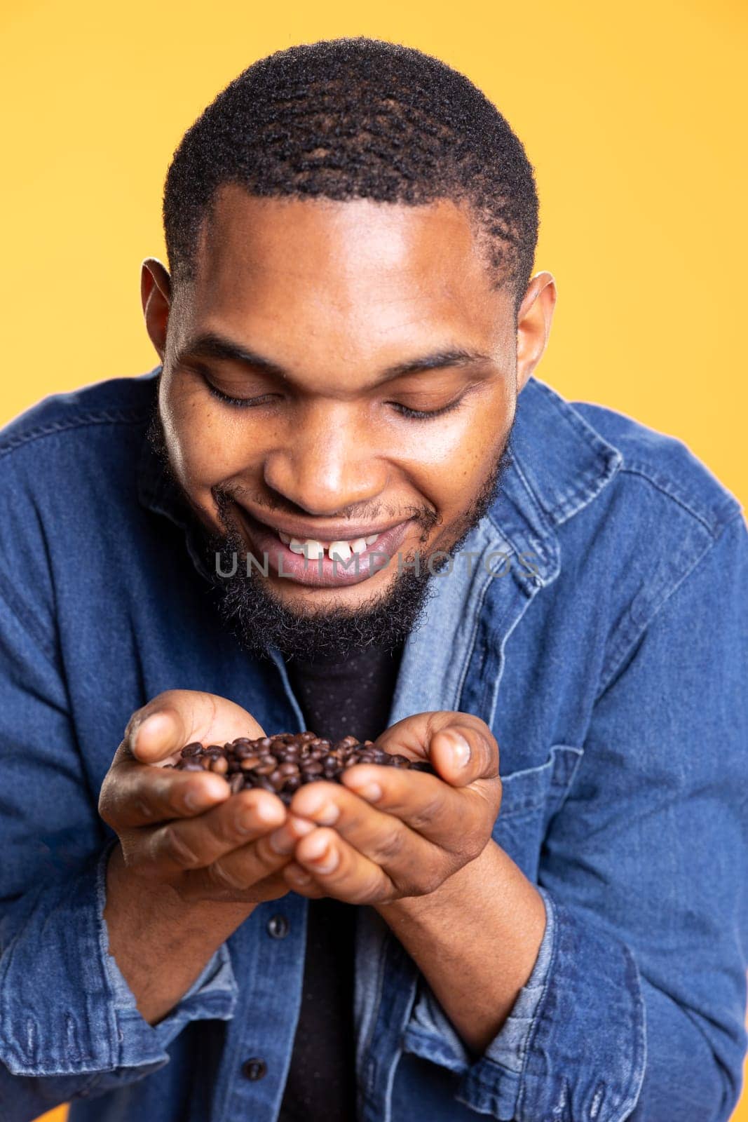 Coffee lover savoring the fresh aromatic black roasted scent, enthusiastic man holding a handful of coffee beans up to his nose and enjoying the c0old brew aroma, delicious flavor.