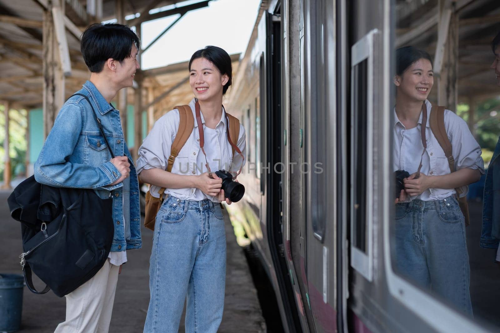 Happy young Asian couple carrying backpacks and cameras preparing to wait for the train at the train station waiting for their vacation trip together. by wichayada