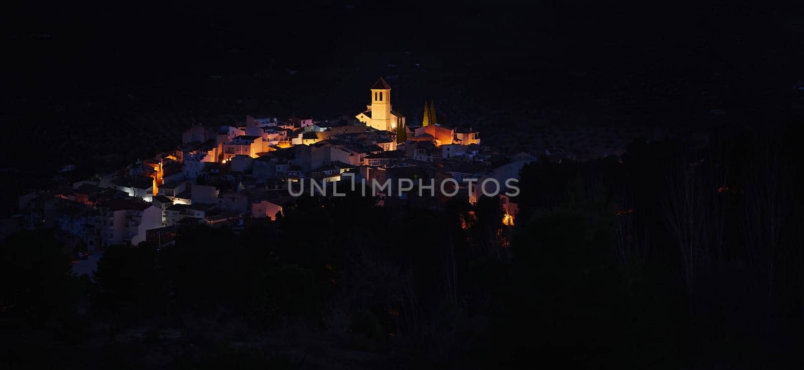 View from the hill of medieval historical village of Quesada in province of Jaen, with the illuminated bell tower and while houses in the night time. Beauty in Spain nature. Travel and tourism concept
