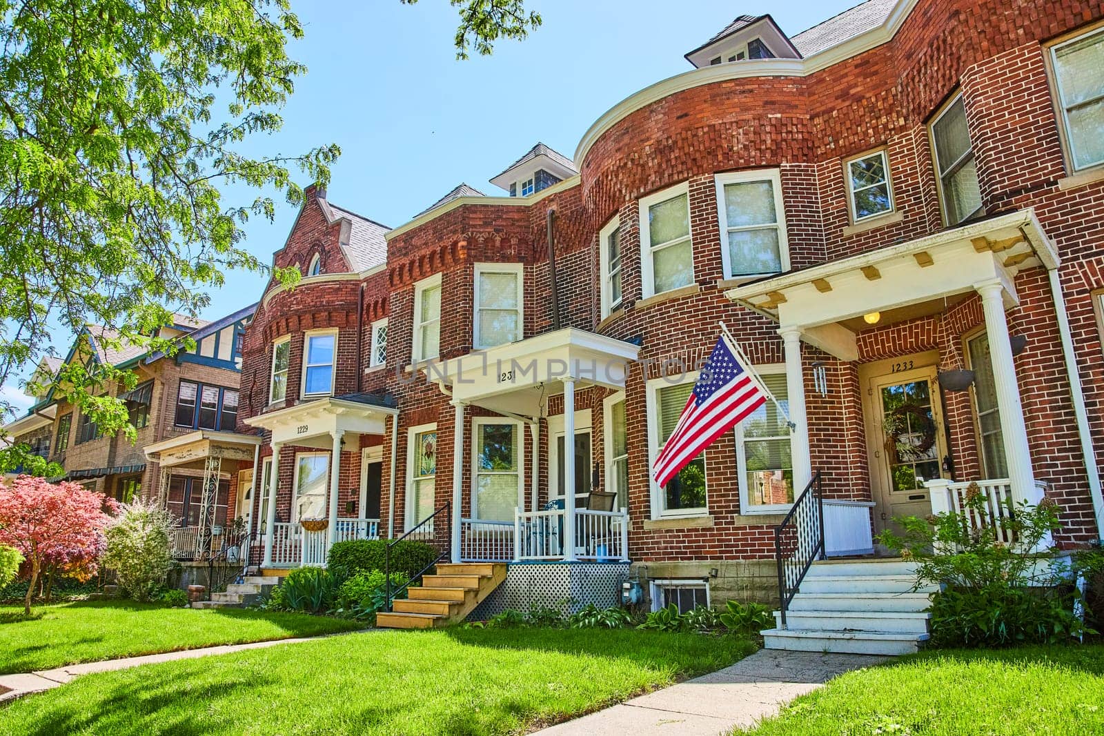 Sunny suburban street in Fort Wayne with traditional brick houses and American flag, symbolizing community and patriotism.