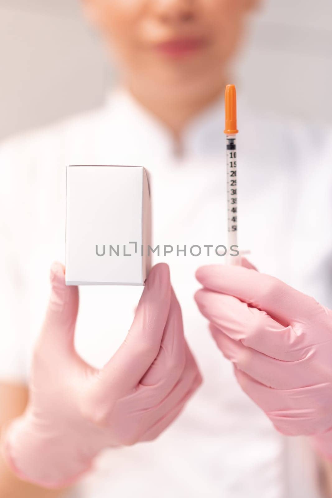 Cosmetologist in pink gloves showing skin lifting injection and mockup drug box. Crop blur dermatologist in white uniform demonstrating product mockup in clinic.