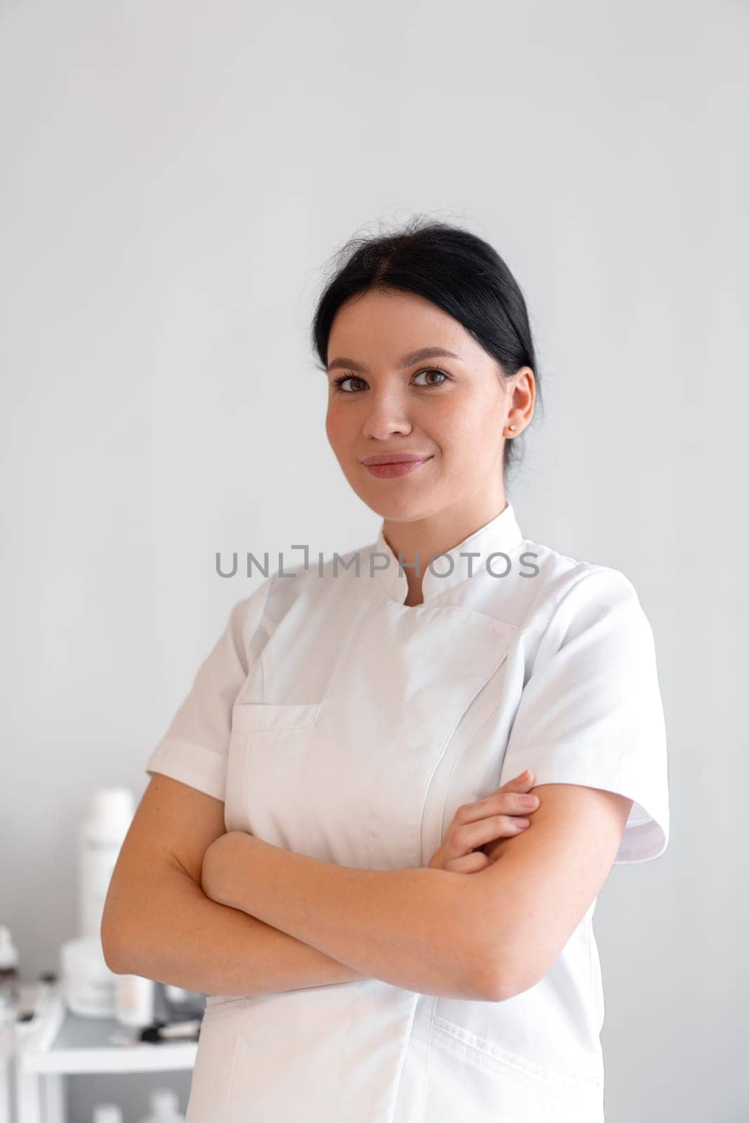 Smiling female cosmetologist standing arms crossed in clinic by andreonegin