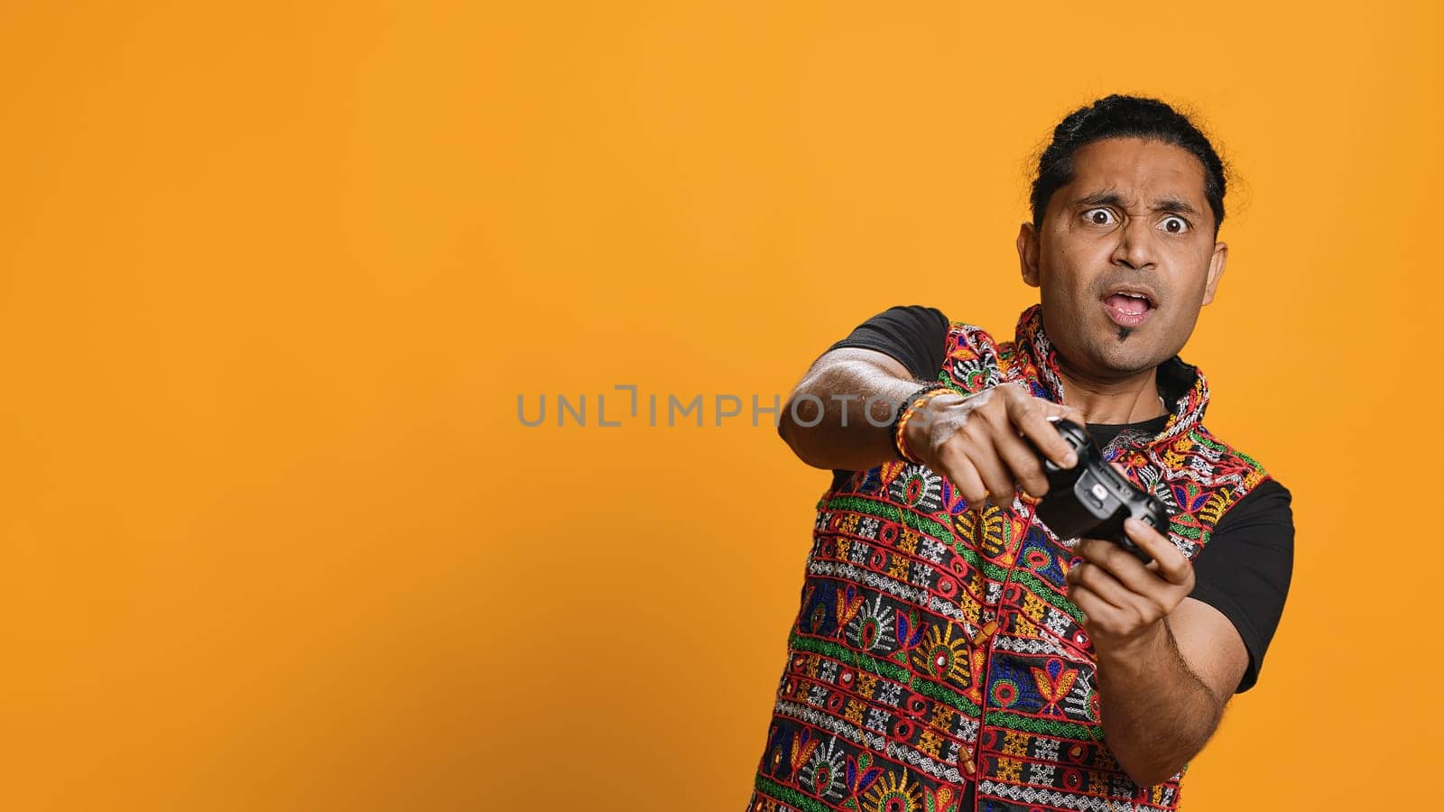 Gamer annoyed after losing online multiplayer videogame, being defeated by rival players. Indian man shocked and gutted after seeing game over message, holding controller, studio background, camera A