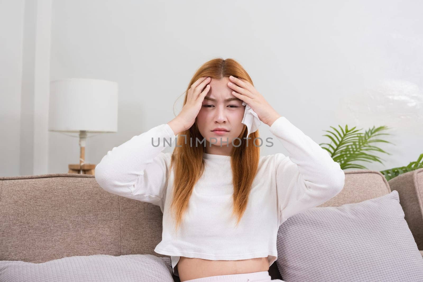 A young Asian woman in the living room was suffering from a headache due to accumulated stress due to health problems and lifestyle problems causing stress disorder..